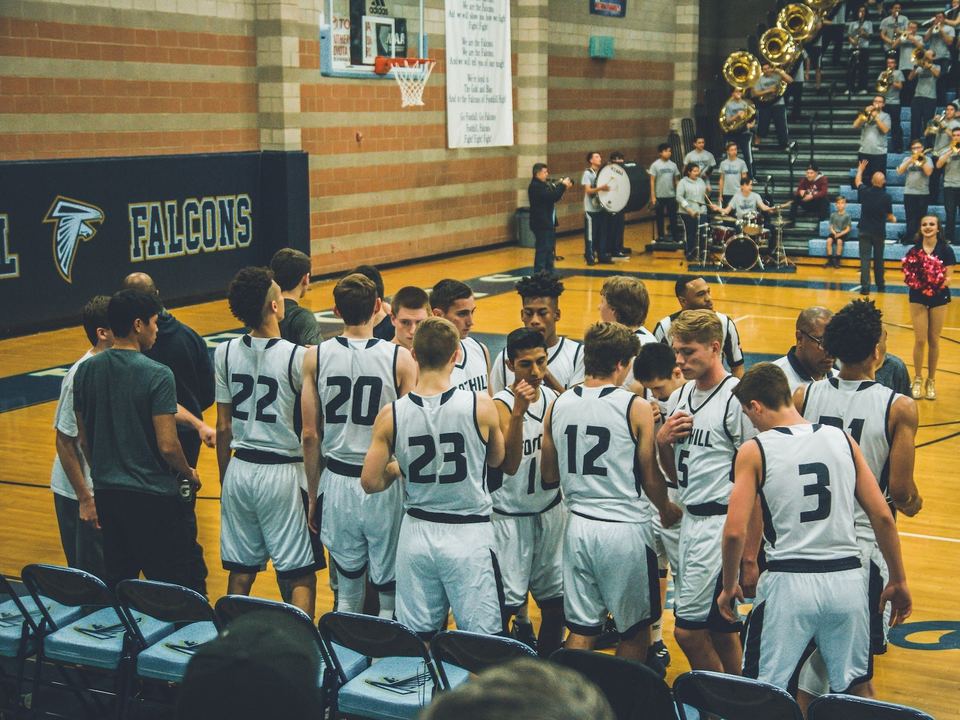 High school basketball team huddled on the court in matching uniforms