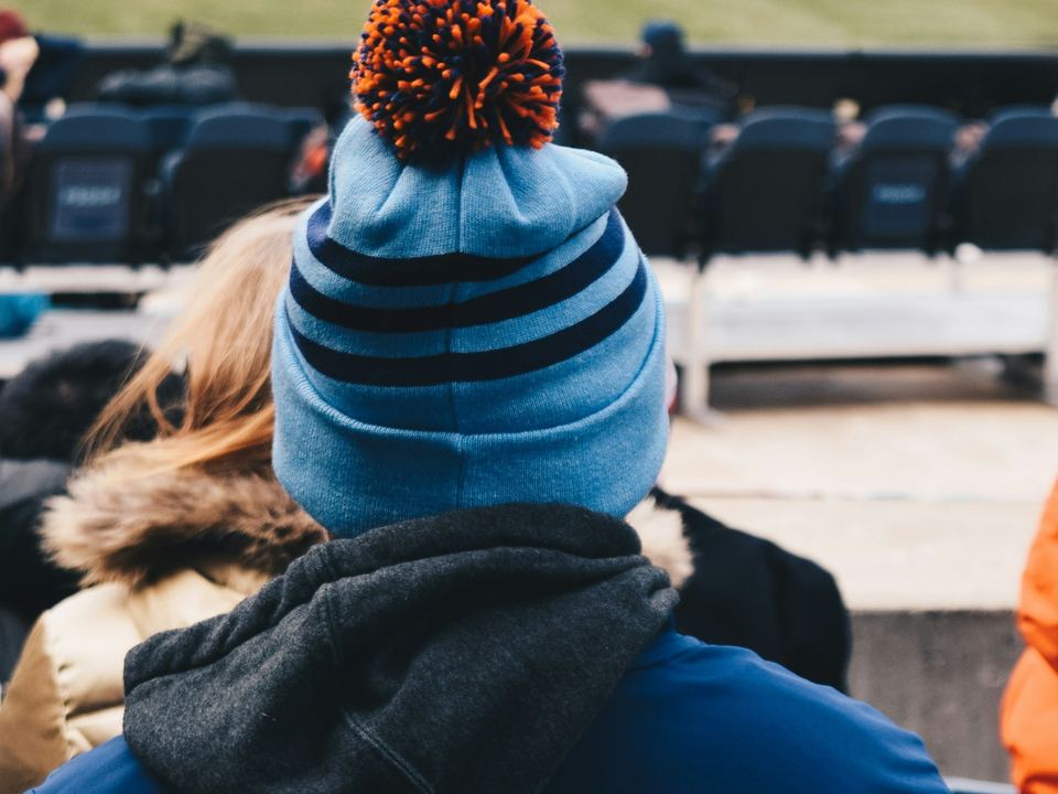 A fan in a striped beanie and hoodie watching from the stands
